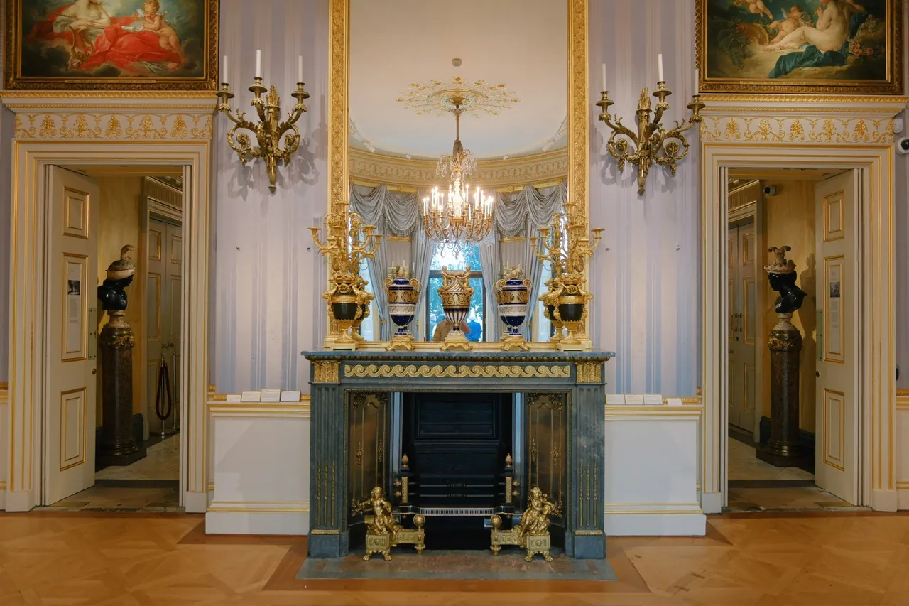 A Wallace Collection room with ivory walls, gilded decoration and a fireplace